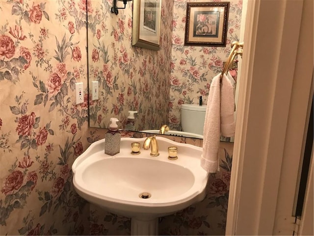 half bathroom with wallpapered walls, a sink, and toilet