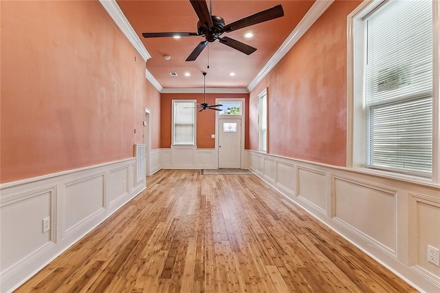 spare room featuring crown molding, a ceiling fan, wainscoting, and a decorative wall