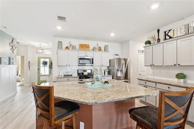kitchen with a kitchen breakfast bar, stainless steel appliances, light wood-type flooring, backsplash, and visible vents