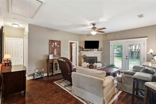 living room featuring ceiling fan, attic access, visible vents, a tiled fireplace, and dark wood-style floors