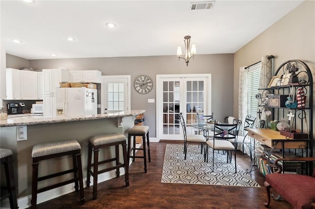 kitchen featuring visible vents, white appliances, a kitchen bar, white cabinetry, and light stone counters