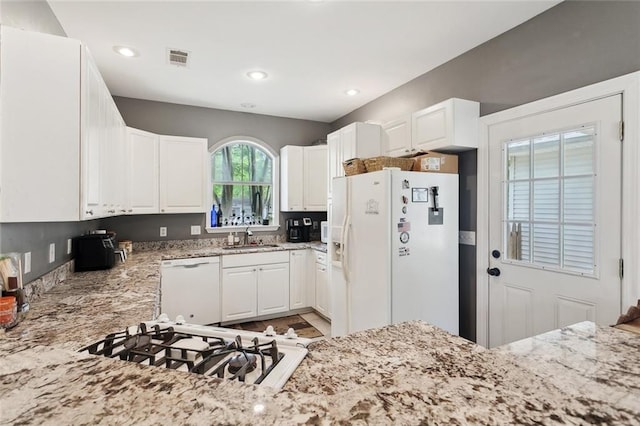 kitchen with visible vents, white appliances, light stone countertops, white cabinetry, and a sink