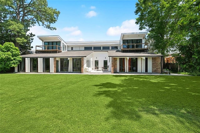 rear view of house featuring a lawn, a patio, brick siding, and a balcony