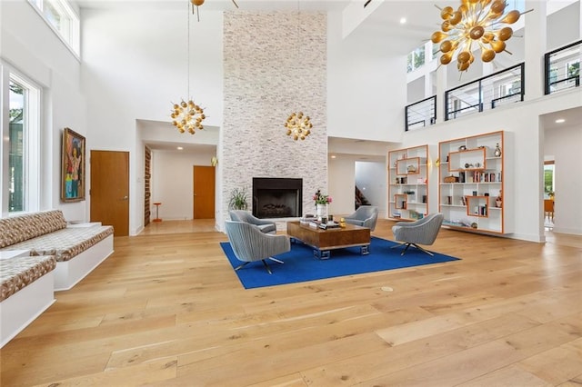 living room with an inviting chandelier, a towering ceiling, hardwood / wood-style flooring, and a large fireplace