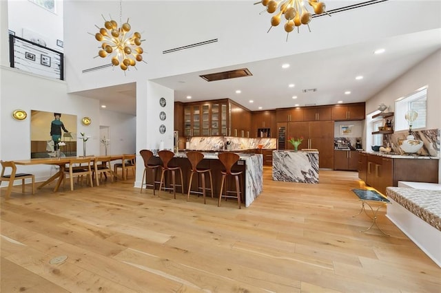 kitchen with a peninsula, light wood-style floors, a kitchen bar, a chandelier, and backsplash