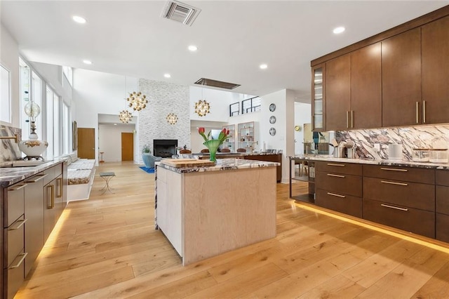 kitchen with backsplash, a kitchen island, visible vents, a large fireplace, and modern cabinets