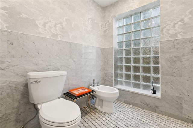 bathroom with tile walls, tile patterned floors, toilet, and a bidet
