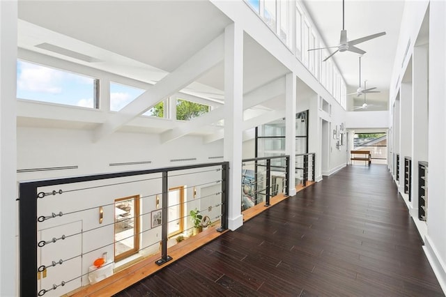 hall with a towering ceiling, wood finished floors, beamed ceiling, baseboards, and an upstairs landing