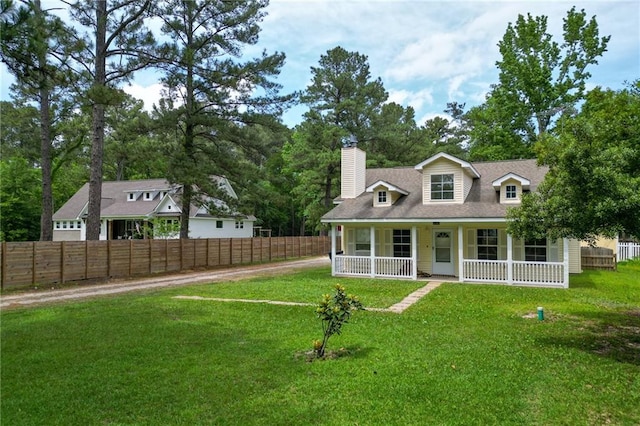 view of front facade with a porch, fence, a chimney, and a front lawn