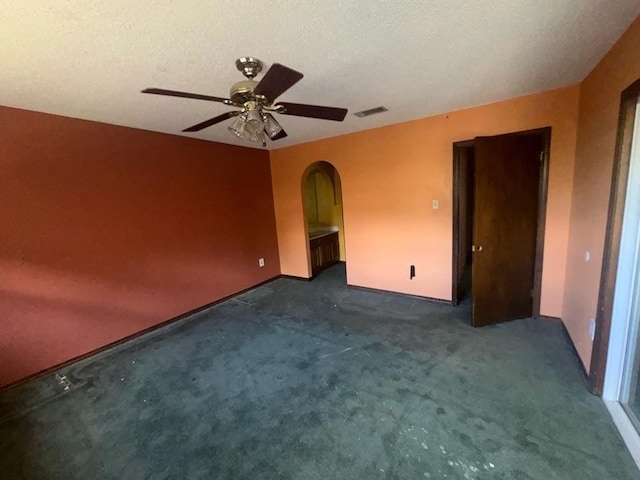 unfurnished room featuring carpet floors, a ceiling fan, visible vents, baseboards, and arched walkways