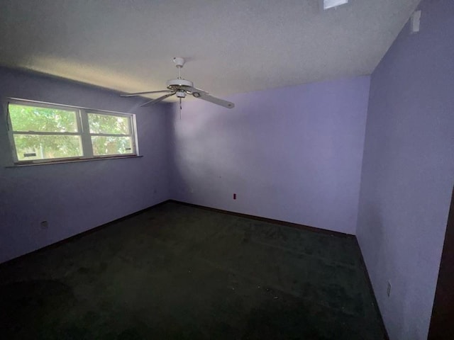 unfurnished room with baseboards, ceiling fan, and dark carpet