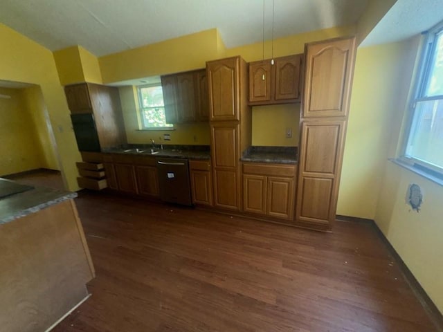 kitchen with brown cabinetry, dark countertops, dishwashing machine, a sink, and dark wood finished floors