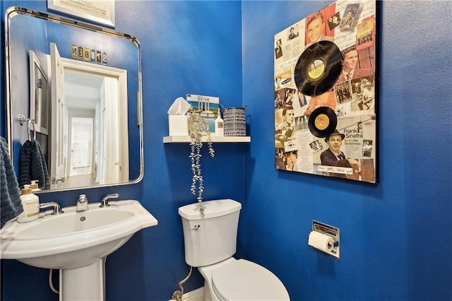 half bath with toilet, baseboards, and a sink