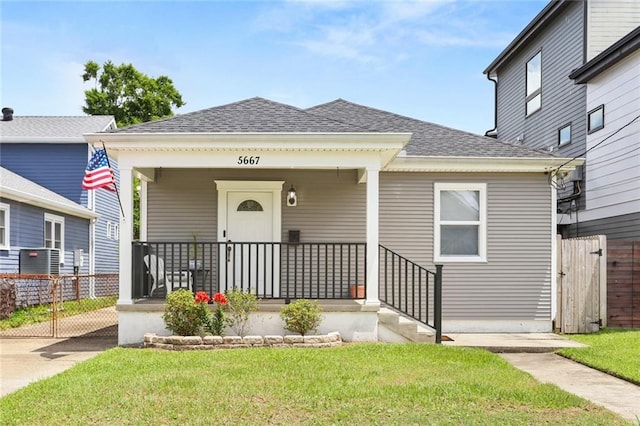 bungalow-style home with covered porch, roof with shingles, fence, cooling unit, and a front lawn