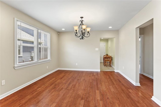 spare room with an inviting chandelier, recessed lighting, baseboards, and wood finished floors