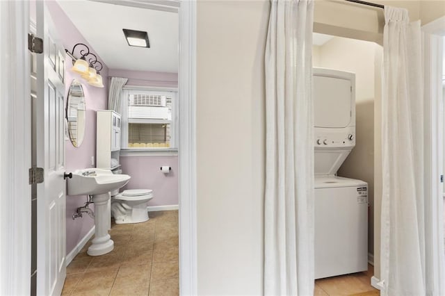 bathroom with toilet, baseboards, tile patterned flooring, and stacked washer and clothes dryer