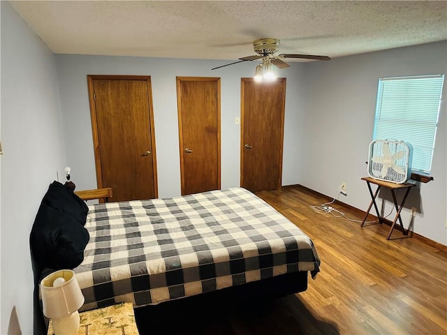 bedroom featuring wood finished floors, two closets, baseboards, ceiling fan, and a textured ceiling