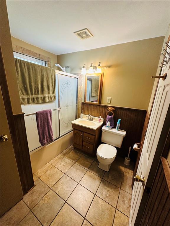 full bathroom with visible vents, bath / shower combo with glass door, tile patterned floors, vanity, and toilet
