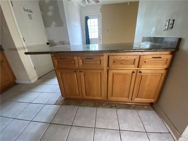 kitchen featuring light tile patterned floors, a peninsula, a ceiling fan, and brown cabinets