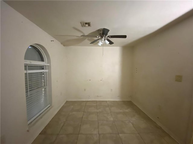 tiled empty room featuring visible vents, baseboards, and ceiling fan