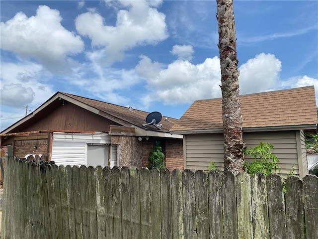 view of side of property featuring roof with shingles and fence