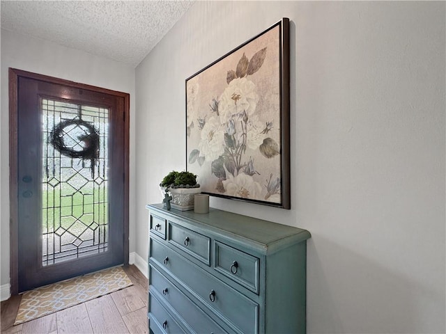 entryway with light wood-type flooring, a textured ceiling, and baseboards