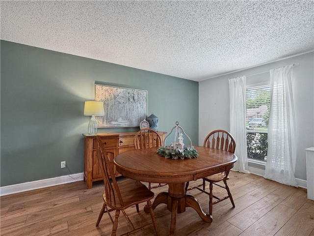 dining space with baseboards, light wood finished floors, and a textured ceiling
