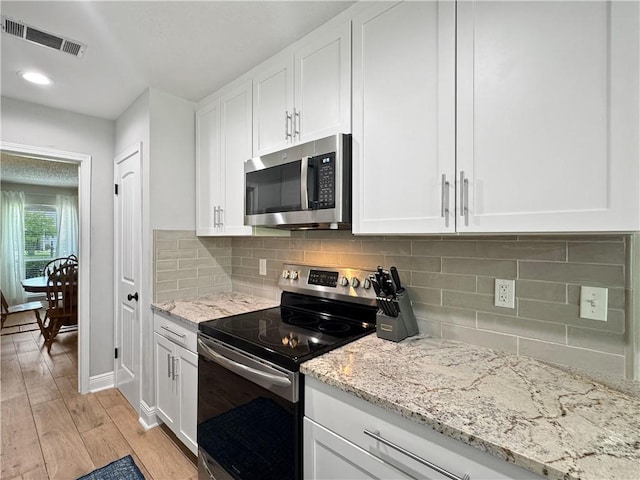 kitchen featuring visible vents, light wood-type flooring, light stone counters, stainless steel appliances, and white cabinetry