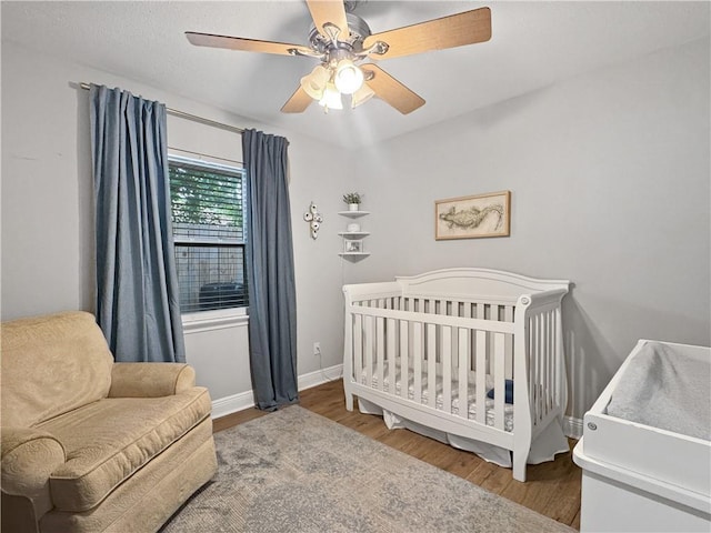 bedroom with baseboards, a ceiling fan, a crib, and wood finished floors