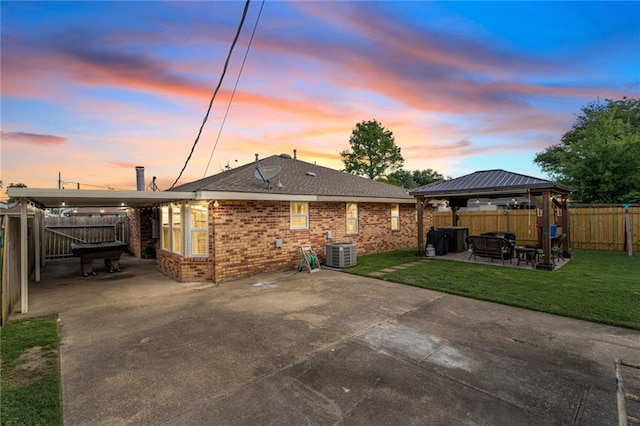 202 River Point Dr, Destrehan, LA 70047 - back of house at dusk featuring brick siding, a gazebo, central AC, a fenced backyard, and a patio