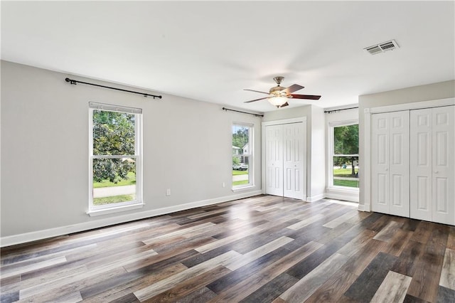 unfurnished bedroom with baseboards, visible vents, multiple windows, and dark wood-type flooring