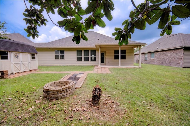 rear view of property with a fire pit, a patio, a yard, a storage shed, and an outbuilding