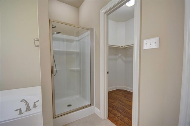 bathroom with a walk in closet, a shower stall, a bath, and wood finished floors