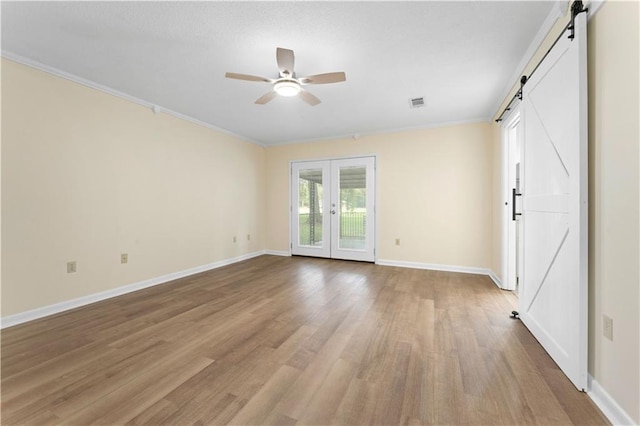 unfurnished room featuring ceiling fan, french doors, a barn door, light wood-style floors, and ornamental molding