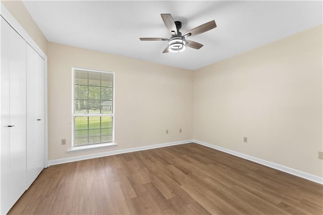 unfurnished bedroom featuring baseboards, a ceiling fan, wood finished floors, and a closet