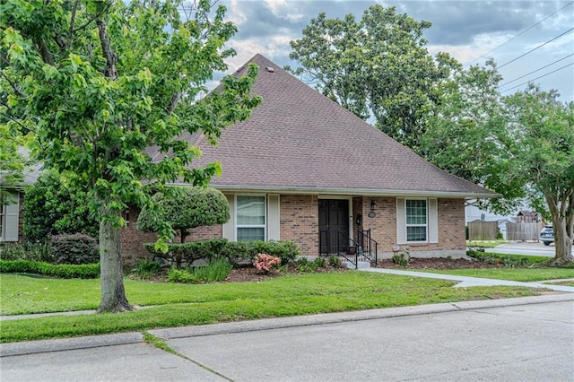 view of front of property featuring roof with shingles, a front yard, and brick siding