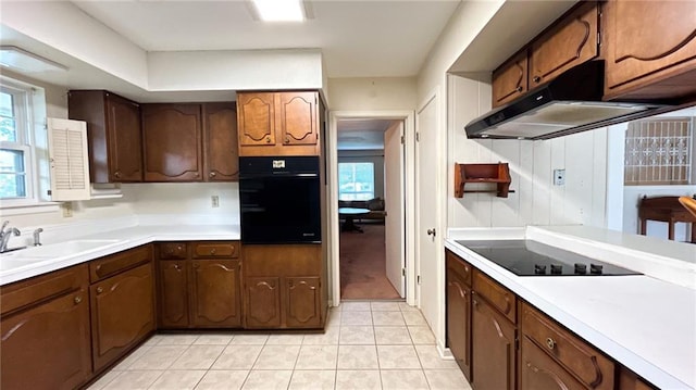 kitchen with light countertops, under cabinet range hood, a sink, light tile patterned floors, and black appliances