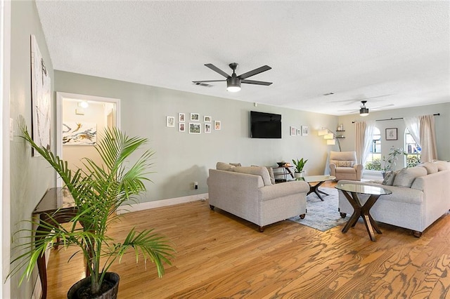 living area featuring ceiling fan, a textured ceiling, visible vents, baseboards, and light wood finished floors