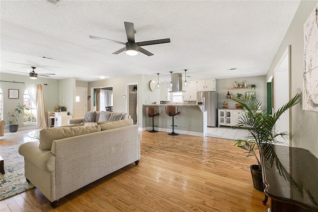 living room with a ceiling fan, a textured ceiling, baseboards, and light wood-style floors