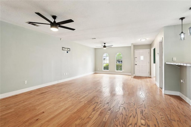 unfurnished living room featuring a ceiling fan, baseboards, visible vents, and light wood-type flooring