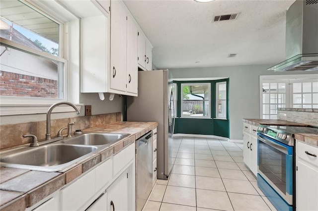 kitchen featuring appliances with stainless steel finishes, a sink, wall chimney exhaust hood, white cabinetry, and light tile patterned floors