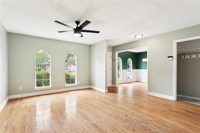 empty room featuring light wood-style floors, a ceiling fan, baseboards, and a textured ceiling