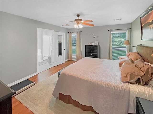 bedroom featuring visible vents, wood finished floors, baseboards, a ceiling fan, and ensuite bath