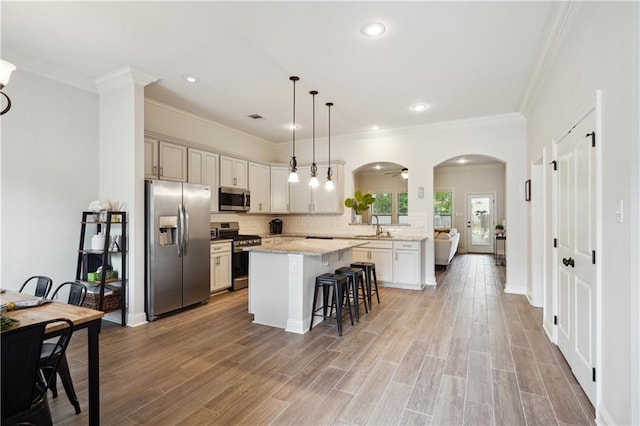 kitchen with appliances with stainless steel finishes, a sink, arched walkways, a kitchen bar, and a kitchen island