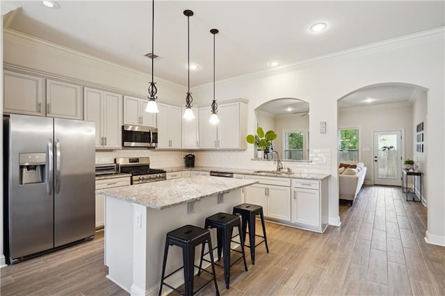 kitchen with appliances with stainless steel finishes, a center island, arched walkways, a sink, and light wood-style floors