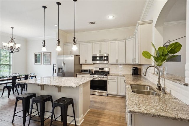 kitchen featuring visible vents, ornamental molding, a center island, a sink, and appliances with stainless steel finishes