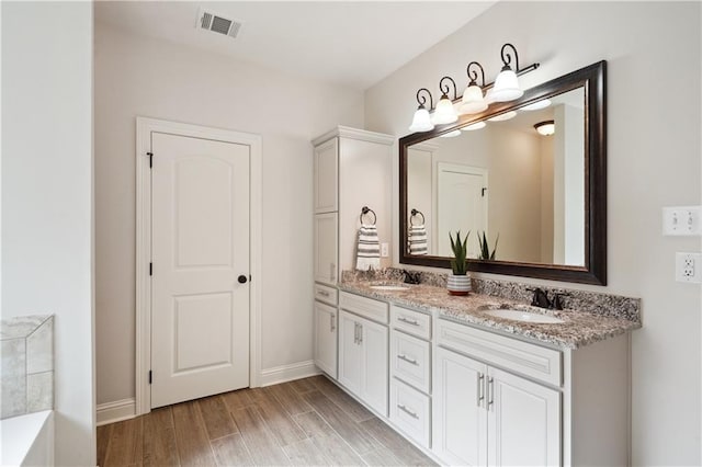 full bath featuring baseboards, visible vents, a sink, and wood finished floors