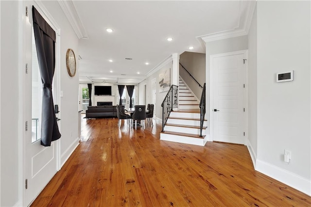 foyer entrance featuring crown molding, a fireplace, stairway, baseboards, and recessed lighting