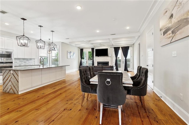 dining area featuring a fireplace, baseboards, ornamental molding, recessed lighting, and light wood-style flooring