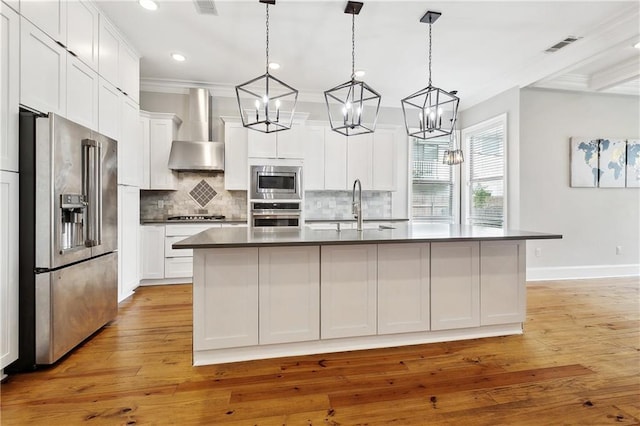 kitchen with wall chimney range hood, crown molding, dark countertops, appliances with stainless steel finishes, and a sink